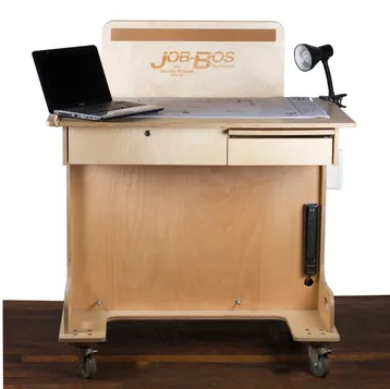 A wooden desk with “JOB BOS,” a laptop, and a lamp on top
